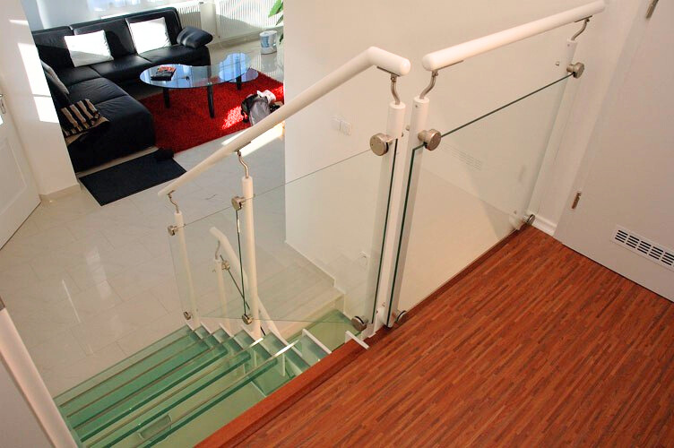 Pohled z horní podesty na skleněné schody Jelínek a obývací pokoj. Bezpečnostní skleněné zábradlí s bílým madlem zajišťuje prosvětlenost celého prostoru.